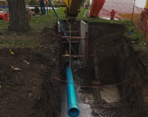 Installing large blue pipeline in deep excavation site.