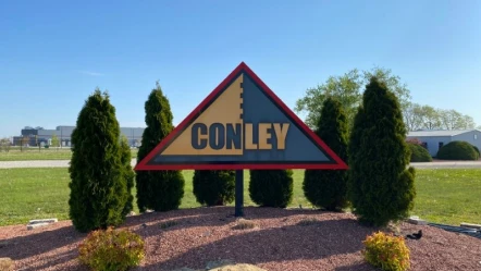 Conley sign surrounded by trees under clear blue sky.