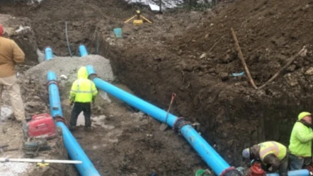 Workers installing large blue pipes in trench.